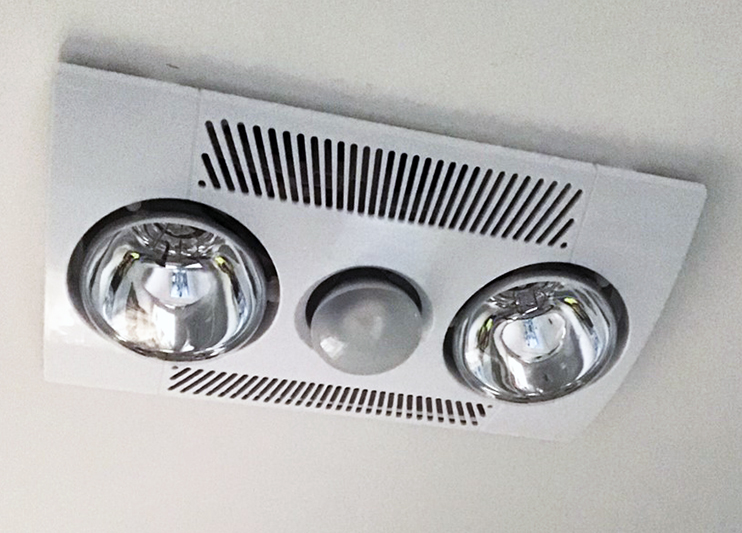 Exhaust fan including two lights,, heater and fan.  White in colour on white ceiling.