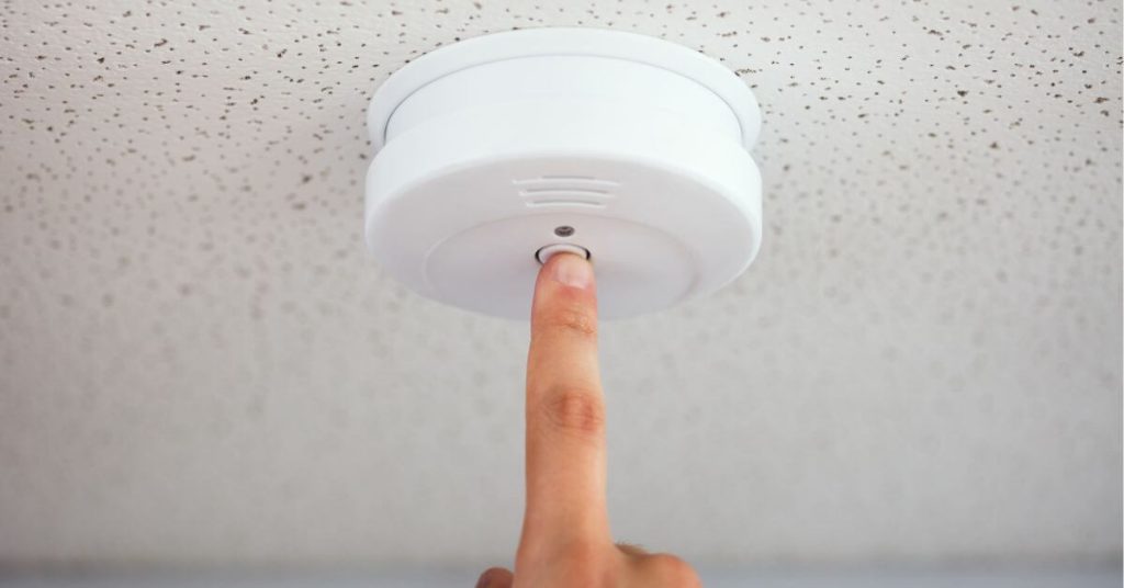 Finger on smoke alarm test button.